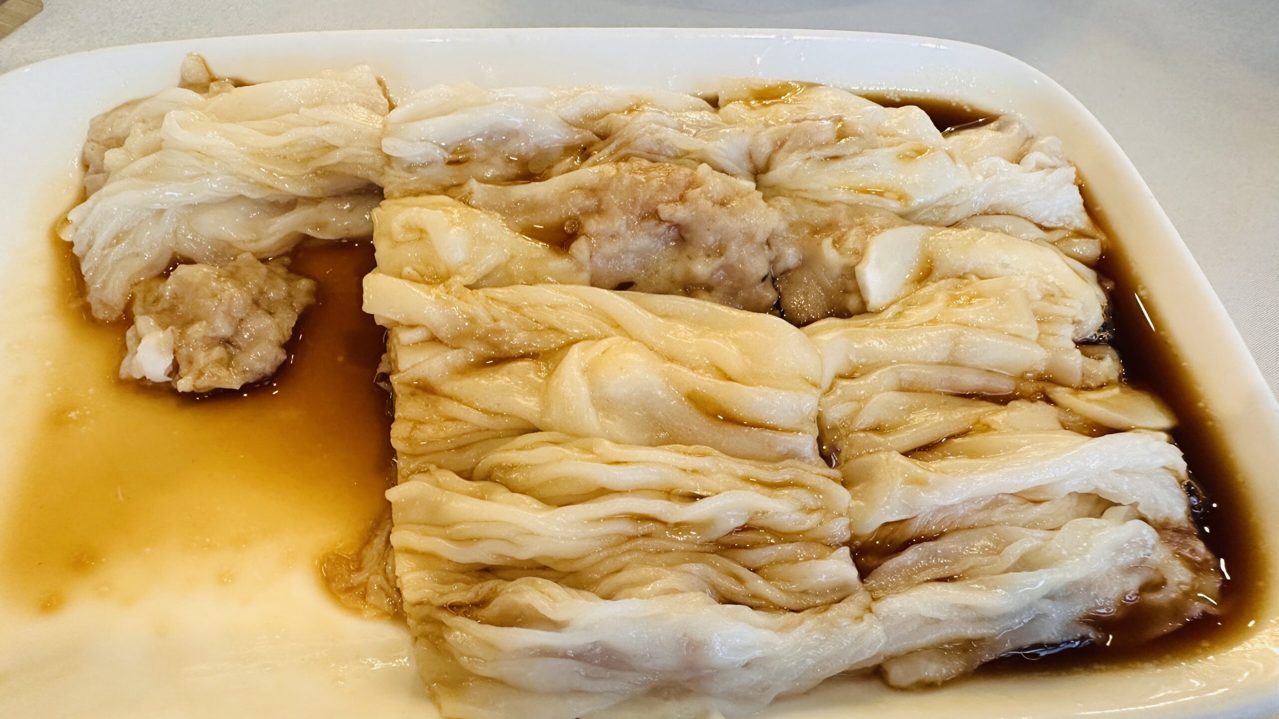 白盘里的肉馅肠粉浸在豉油中，薄滑粉皮层层叠放。