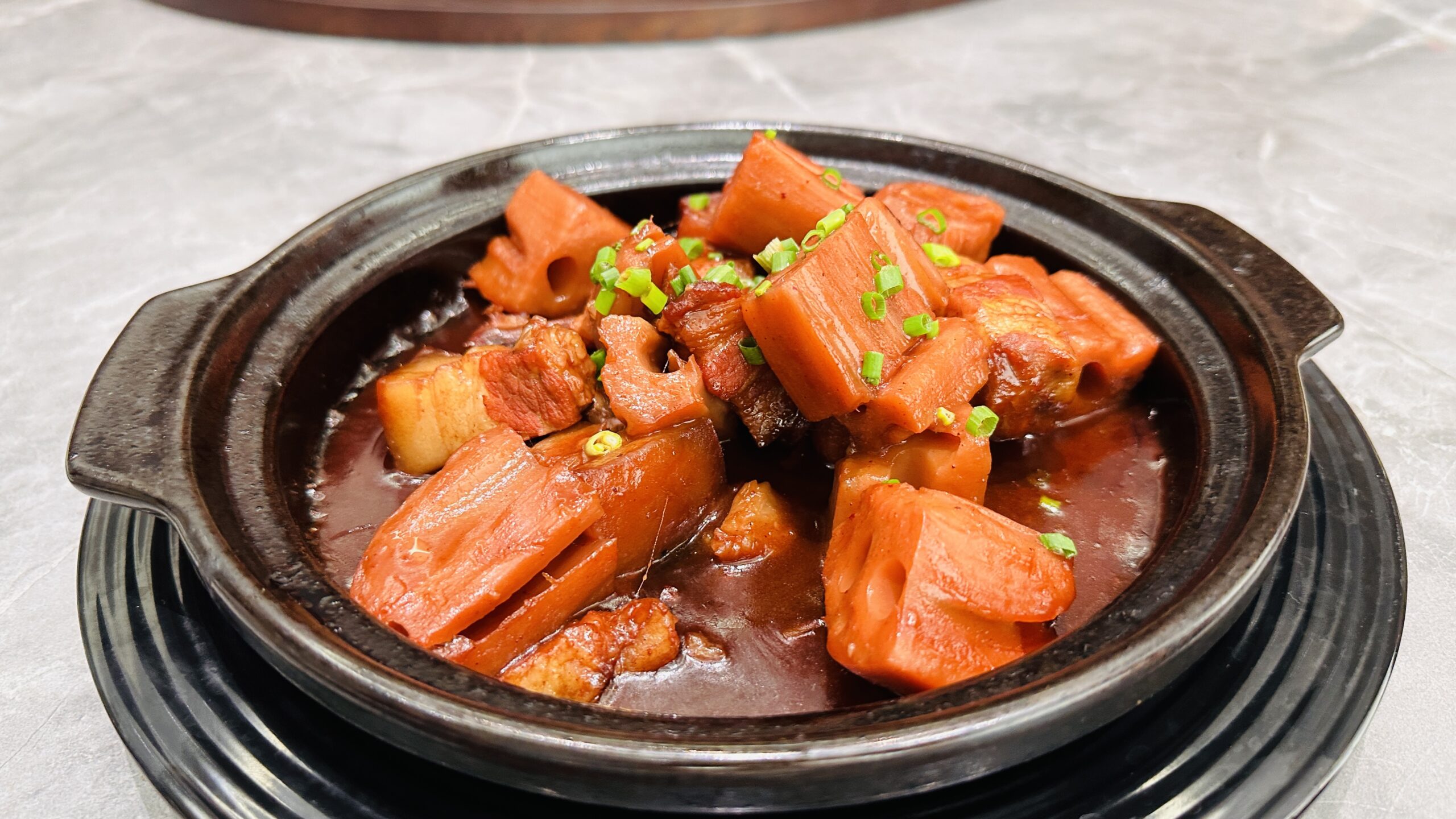 黑色砂锅里是莲藕焖五花肉，酱色汤汁裹住大块食材。