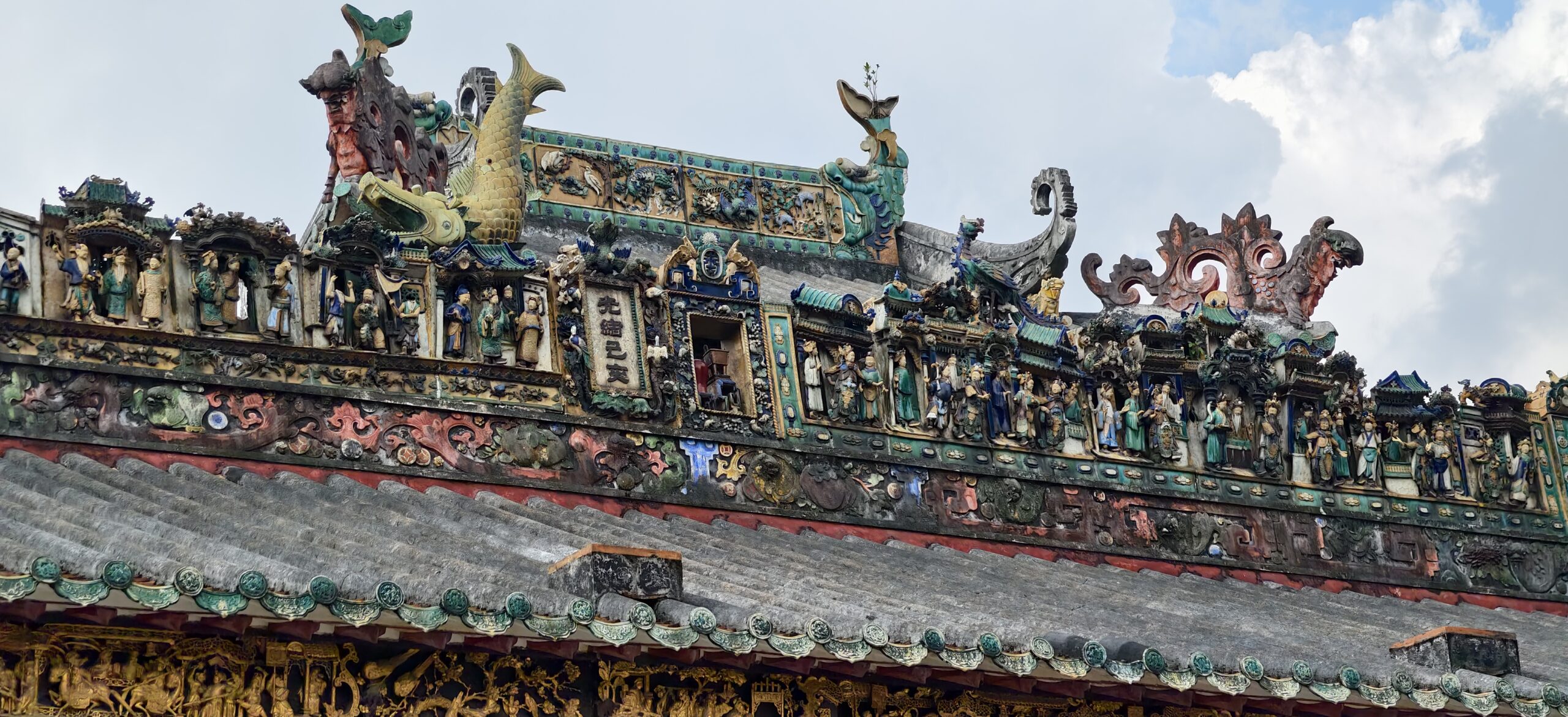 蓝天下的彩色陶塑屋脊横贯画面，人物、鱼兽与花饰连成一线。